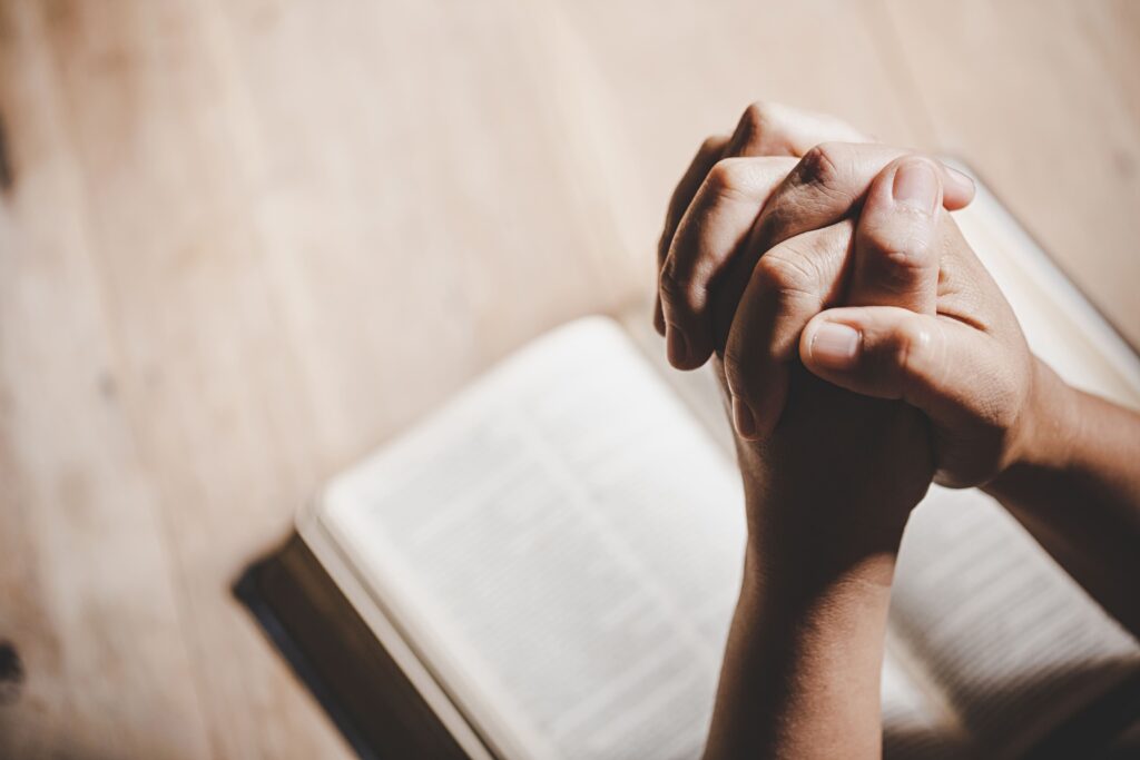Deux main jointes qui prient au dessus d'une bible ouverte